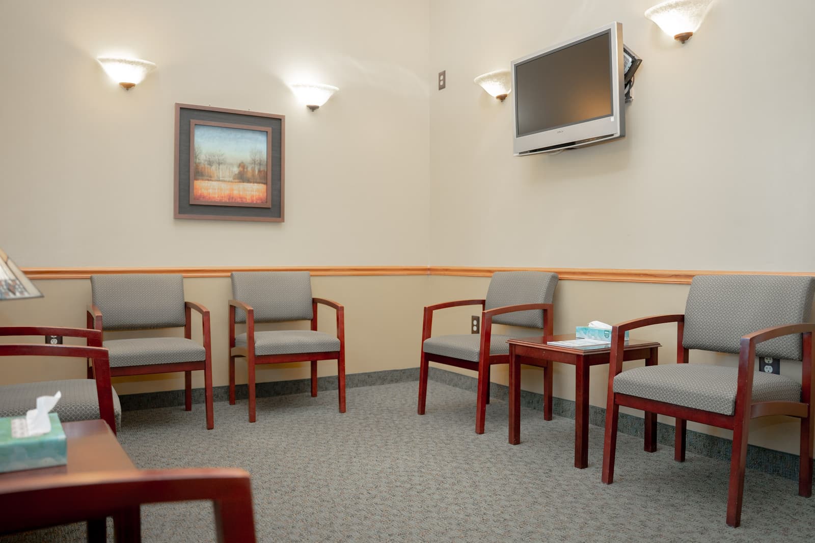 Waiting room with cushioned chairs and a wall-mounted TV